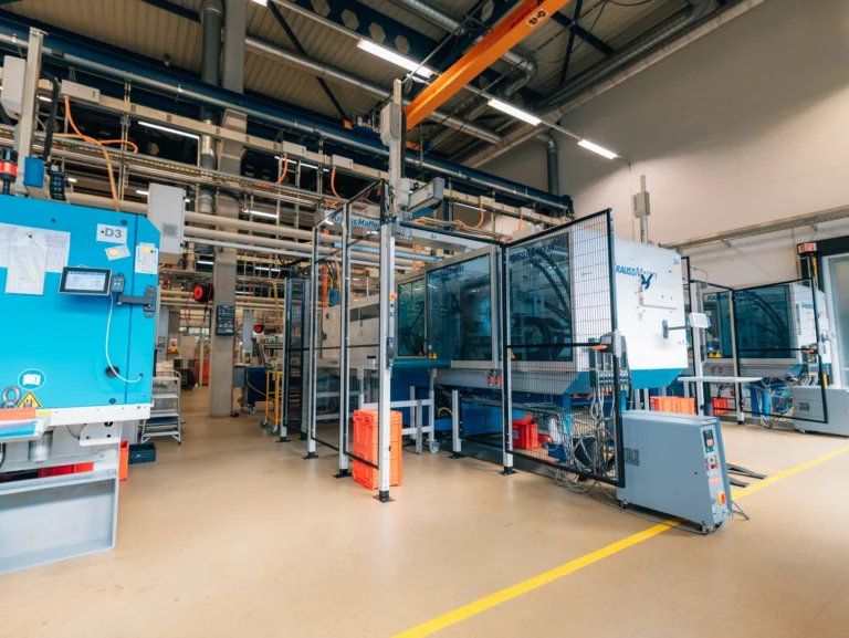 Produktionshalle mit Spritzgiesszellen, Sicherheitsumhausungen und Hallenkran fuer effiziente Kunststofffertigung