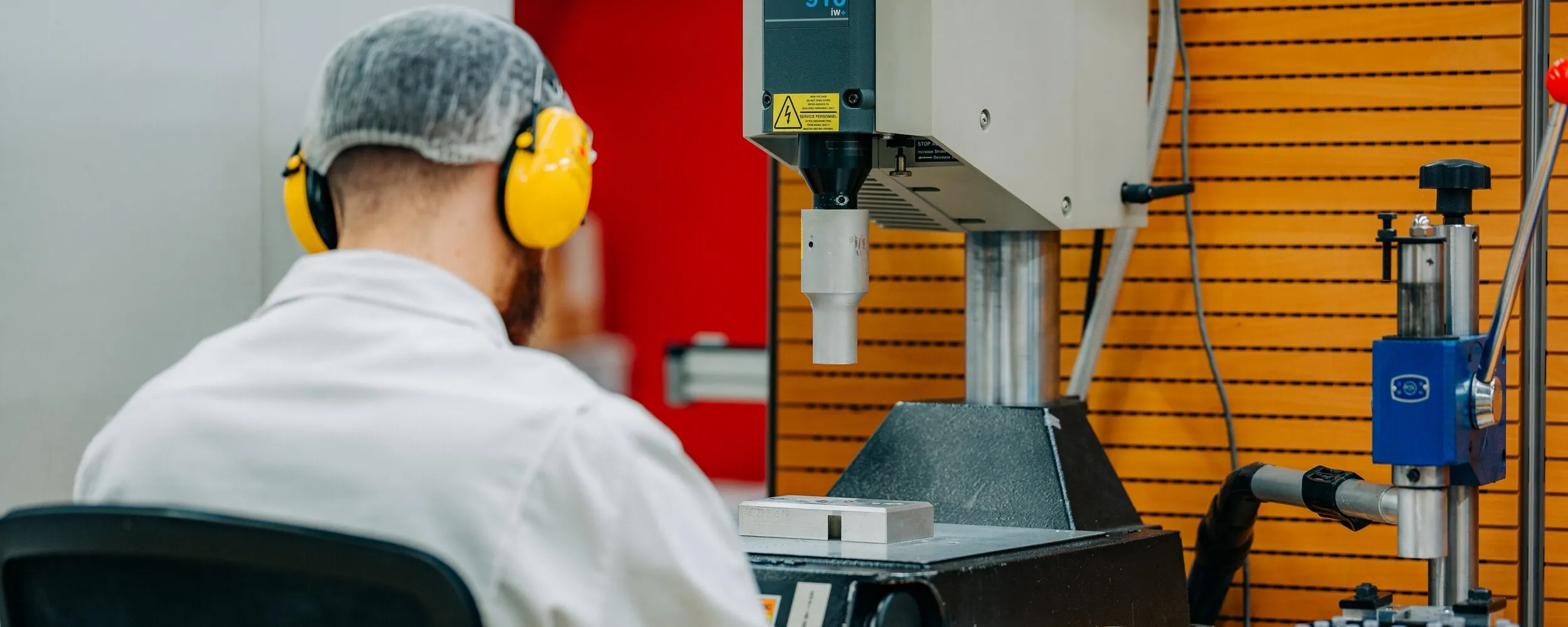 An employee wearing hearing protection at an industrial machine used to process plastic components.